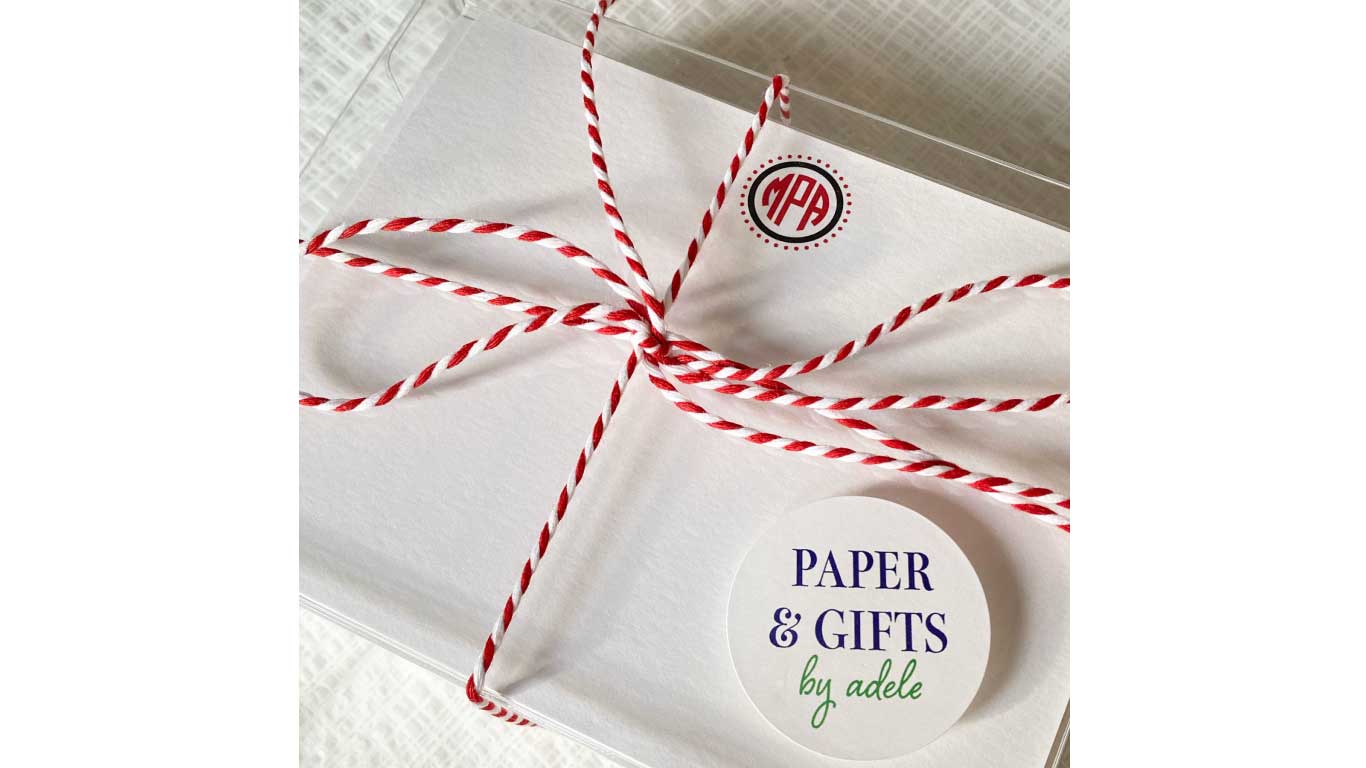 image of white stationery card with red and black monogram in a clear box with red twine wrapping the box